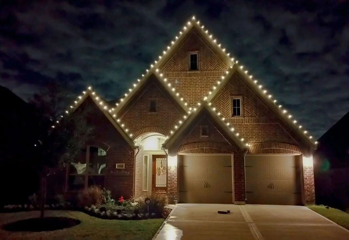Brick home with warm white Christmas lights tracing the front-facing roof peaks